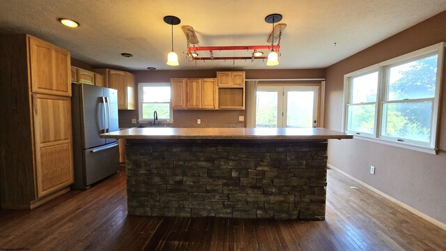 kitchen featuring pendant lighting, sink, a kitchen island, stainless steel fridge, and dark wood-type flooring