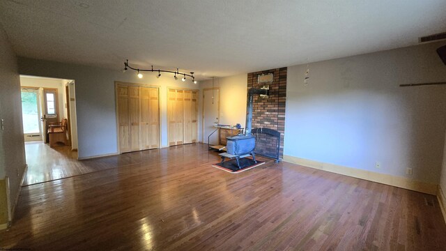 unfurnished living room with a wood stove, a textured ceiling, track lighting, brick wall, and wood-type flooring