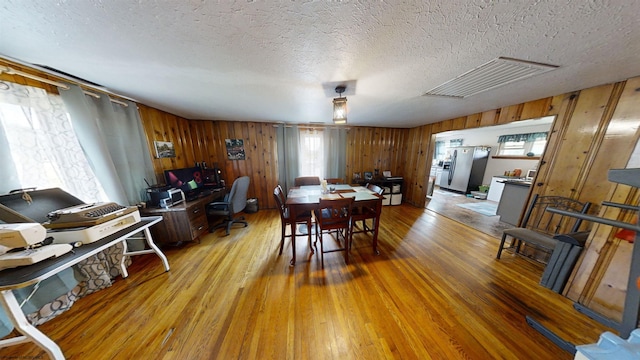 dining room with wooden walls, a textured ceiling, and hardwood / wood-style flooring