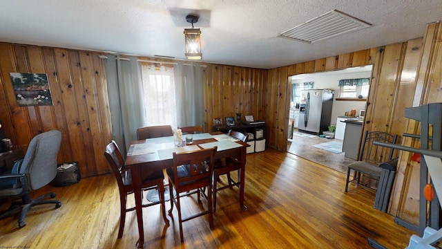 dining room featuring hardwood / wood-style flooring, wooden walls, and a textured ceiling