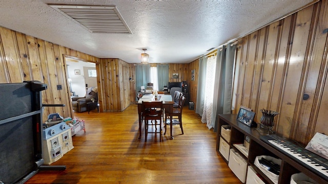 dining space with wood walls, a textured ceiling, and hardwood / wood-style flooring