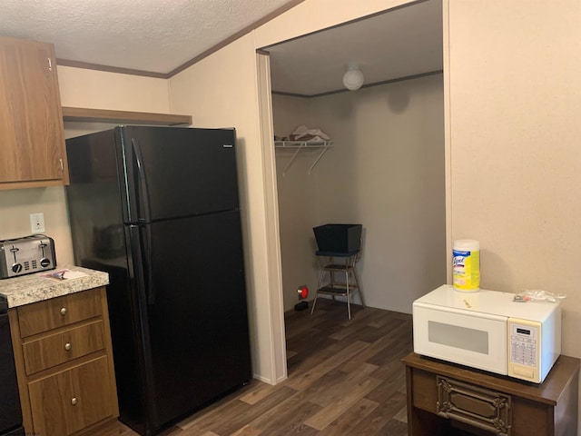 kitchen with a textured ceiling, dark wood-type flooring, ornamental molding, and black refrigerator