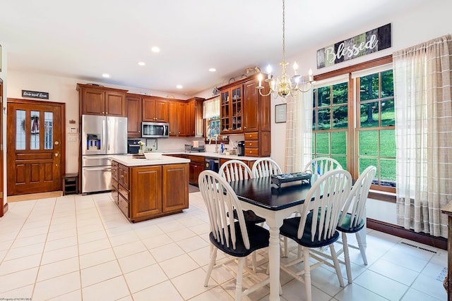 kitchen with decorative light fixtures, a kitchen island, an inviting chandelier, appliances with stainless steel finishes, and light tile patterned floors