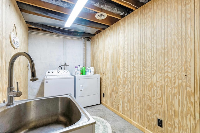 clothes washing area with washer and clothes dryer, sink, and wood walls