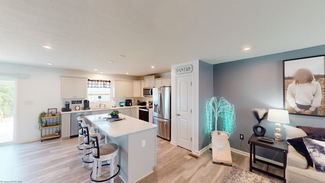 kitchen featuring a breakfast bar, appliances with stainless steel finishes, white cabinets, a kitchen island, and light wood-type flooring