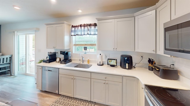 kitchen featuring appliances with stainless steel finishes, sink, light hardwood / wood-style flooring, and white cabinets