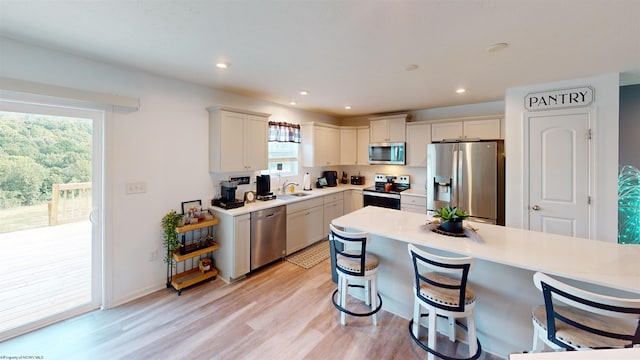 kitchen with white cabinetry, light hardwood / wood-style flooring, stainless steel appliances, and a breakfast bar area