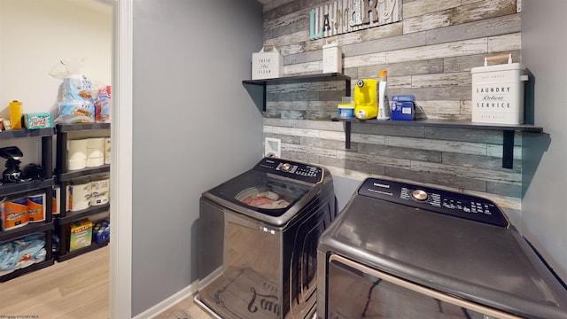 clothes washing area with wooden walls, independent washer and dryer, and light wood-type flooring