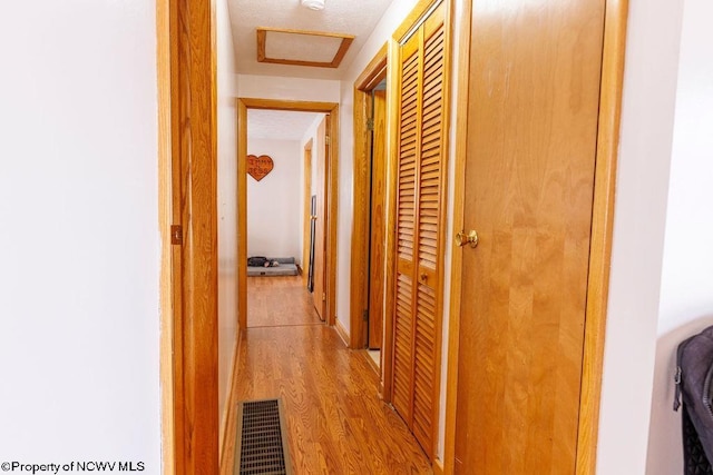 hallway with light hardwood / wood-style flooring and a textured ceiling