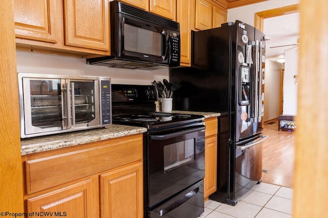 kitchen featuring black appliances, light stone counters, and light wood-type flooring