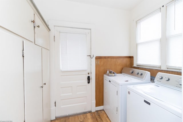 clothes washing area with washing machine and clothes dryer, a wealth of natural light, and light wood-type flooring