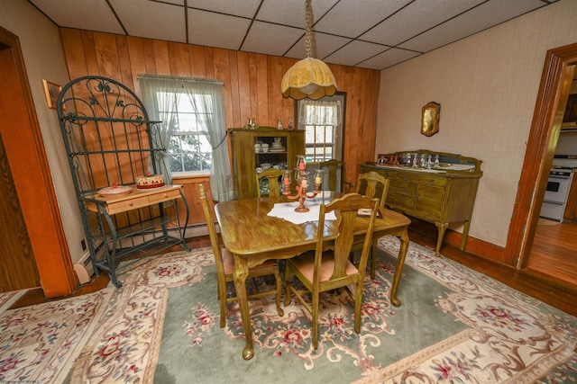 dining area featuring wood walls, a drop ceiling, hardwood / wood-style floors, and baseboard heating