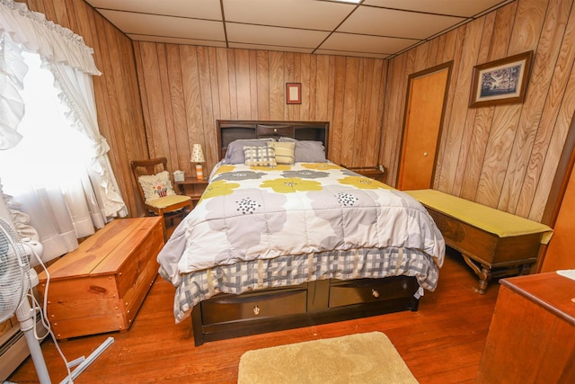 bedroom with a drop ceiling, wooden walls, and hardwood / wood-style floors