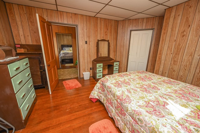 bedroom with wood-type flooring, wood walls, and a paneled ceiling