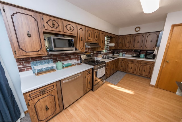 kitchen featuring stainless steel appliances, sink, tasteful backsplash, and light wood-type flooring