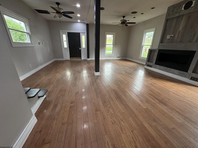 unfurnished living room featuring ceiling fan, a fireplace, hardwood / wood-style floors, and plenty of natural light