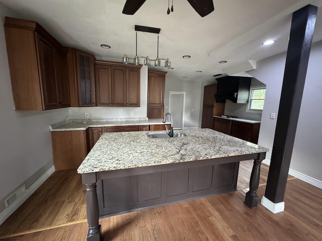 kitchen with wood-type flooring, light stone countertops, sink, and a center island with sink