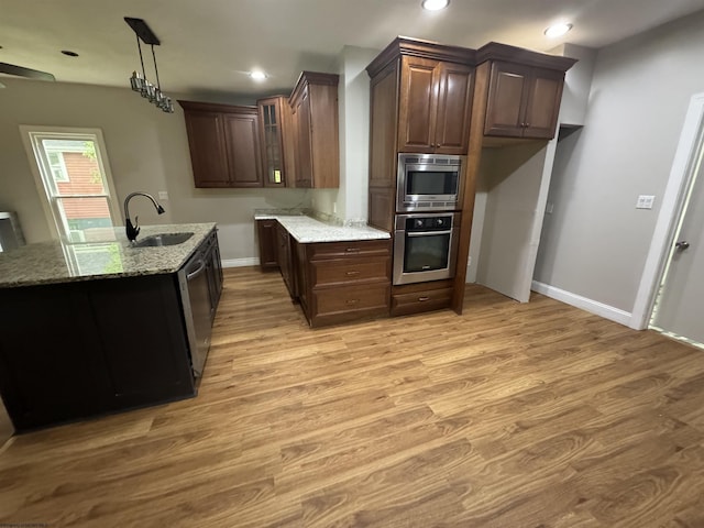 kitchen featuring pendant lighting, sink, stainless steel appliances, light stone counters, and light hardwood / wood-style floors