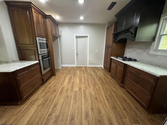 kitchen featuring dark brown cabinets, stainless steel appliances, light stone counters, ventilation hood, and light hardwood / wood-style floors