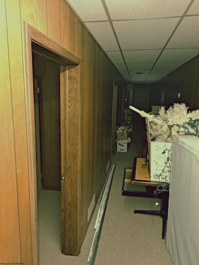 hallway with a paneled ceiling and wood walls