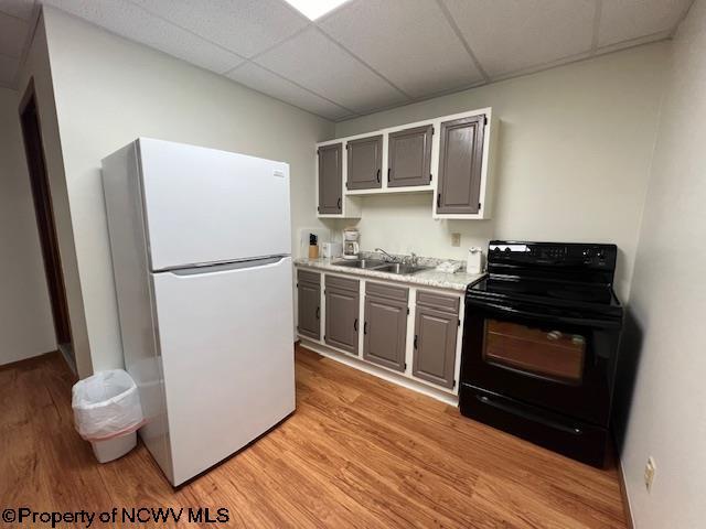 kitchen with black / electric stove, gray cabinetry, a sink, light countertops, and freestanding refrigerator