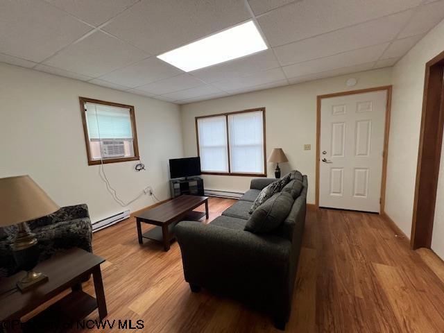 living area with a paneled ceiling, a baseboard heating unit, and wood finished floors