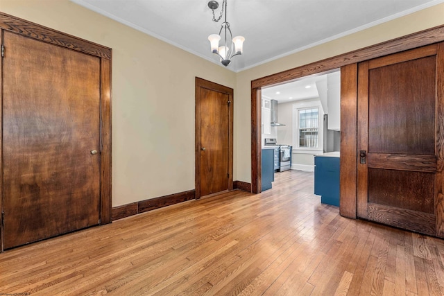 empty room featuring an inviting chandelier, crown molding, and light hardwood / wood-style floors