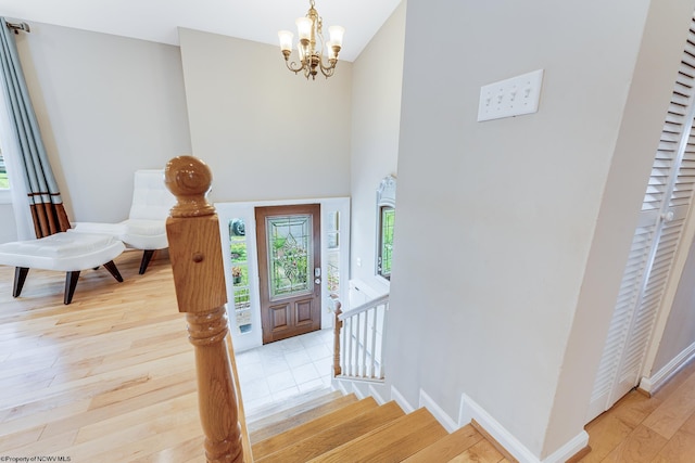 foyer entrance with a towering ceiling, light wood-type flooring, and an inviting chandelier