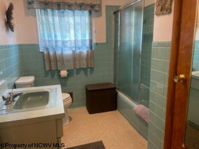 full bathroom featuring vanity, tile walls, enclosed tub / shower combo, and toilet