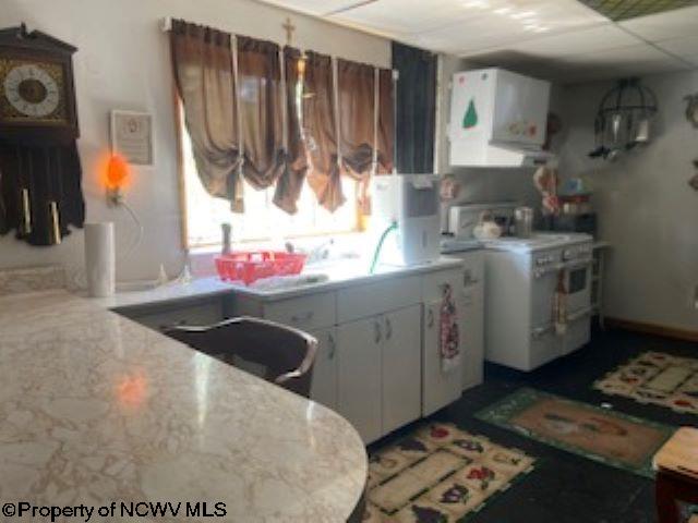 kitchen with electric stove, light stone countertops, white cabinets, and a paneled ceiling