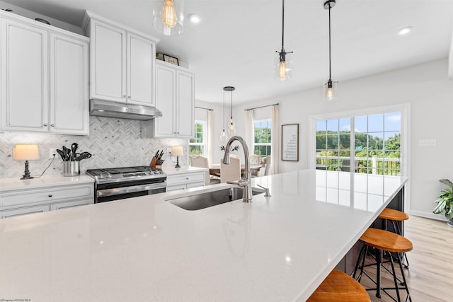 kitchen featuring a kitchen bar, sink, stainless steel range with gas stovetop, light hardwood / wood-style flooring, and decorative light fixtures