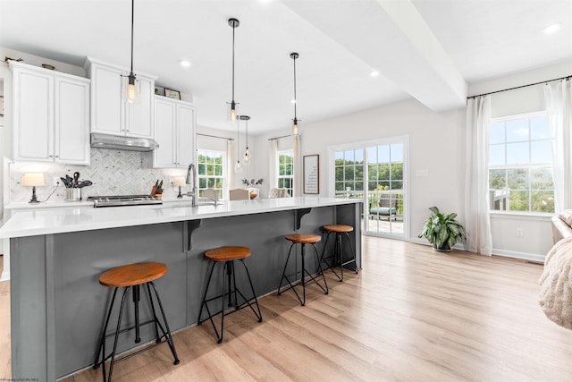 kitchen featuring light wood-type flooring, a kitchen breakfast bar, a large island with sink, and decorative backsplash