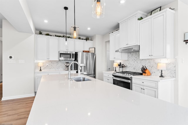 kitchen featuring tasteful backsplash, light wood-type flooring, stainless steel appliances, and decorative light fixtures