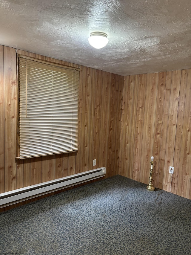 carpeted spare room with wood walls, a textured ceiling, and baseboard heating