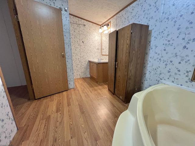 bathroom featuring crown molding, a textured ceiling, vanity, hardwood / wood-style floors, and a washtub