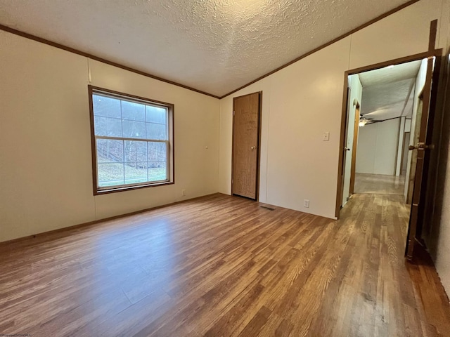 unfurnished bedroom featuring crown molding, light hardwood / wood-style floors, vaulted ceiling, and a textured ceiling