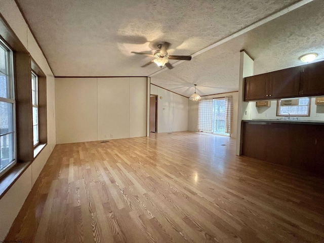 unfurnished living room with vaulted ceiling, ceiling fan with notable chandelier, light wood-type flooring, crown molding, and a textured ceiling