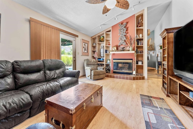 living area with built in shelves, light wood-style flooring, vaulted ceiling, a textured ceiling, and ceiling fan