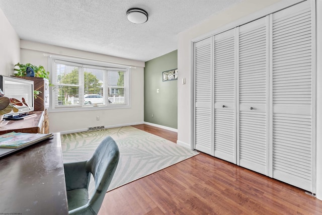 office space with a textured ceiling, wood finished floors, visible vents, and baseboards