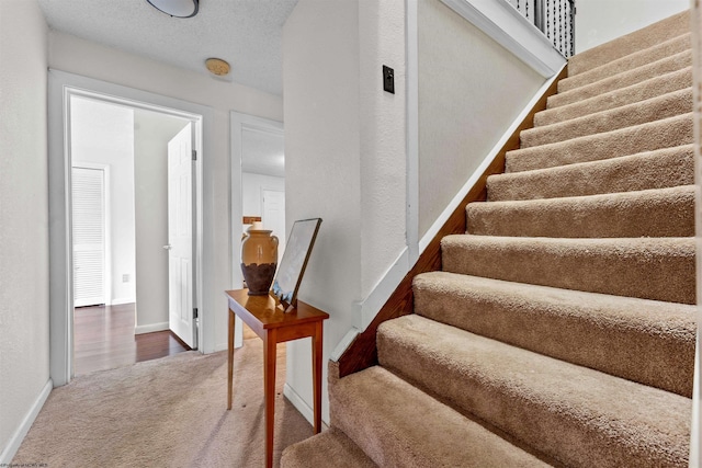 stairway with carpet floors, baseboards, and a textured ceiling