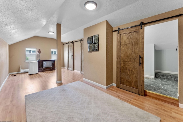 bonus room featuring a barn door, baseboards, lofted ceiling, wood finished floors, and a textured ceiling