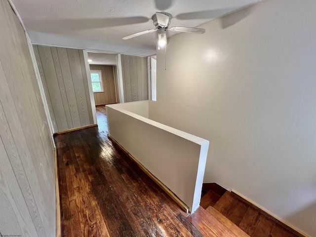 hall featuring wood walls, dark wood finished floors, and an upstairs landing