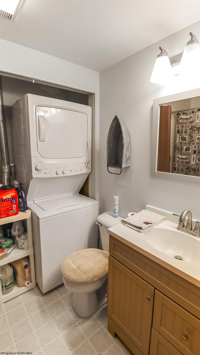 bathroom featuring tile patterned floors, stacked washer / dryer, vanity, and toilet