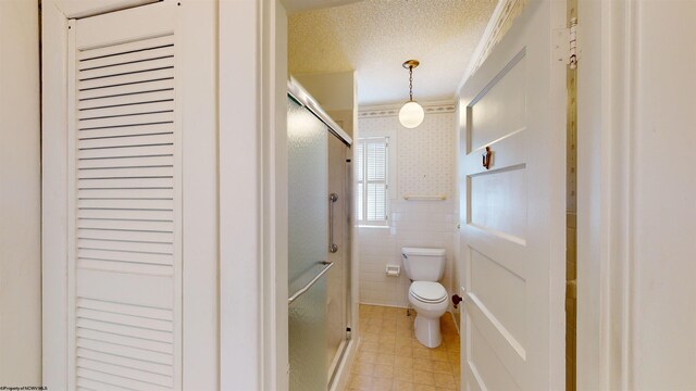 bathroom featuring a textured ceiling, walk in shower, toilet, crown molding, and tile patterned flooring