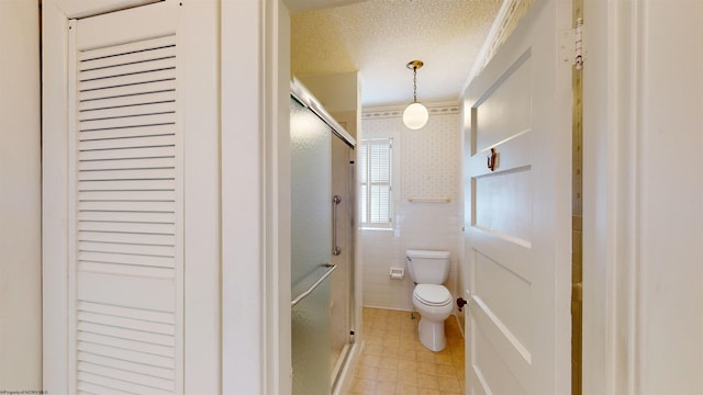 bathroom featuring toilet, crown molding, a textured ceiling, tile walls, and a shower with door