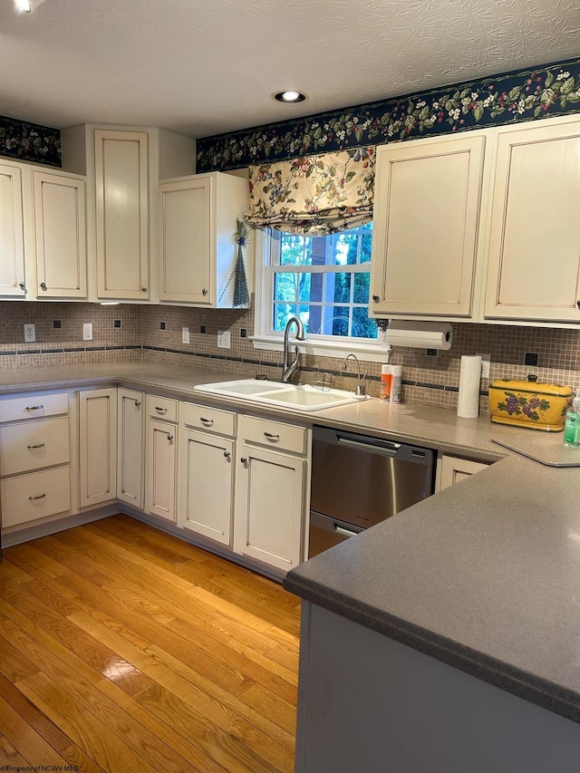 kitchen with tasteful backsplash, stainless steel dishwasher, white cabinetry, light hardwood / wood-style flooring, and sink