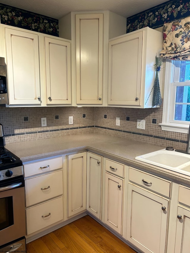 kitchen with white cabinets, light wood-type flooring, gas stove, sink, and tasteful backsplash