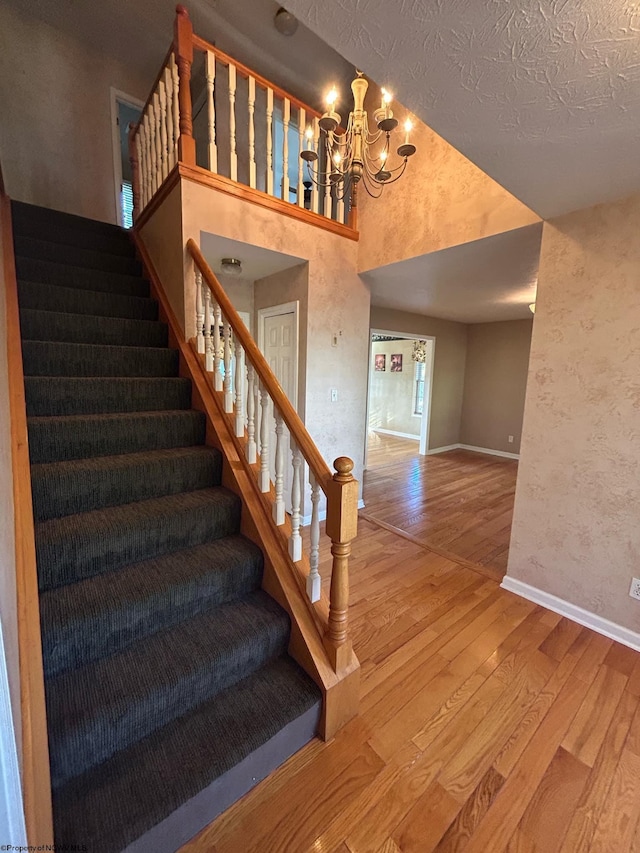 stairs with hardwood / wood-style floors, a textured ceiling, a chandelier, and a high ceiling