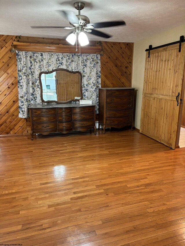 unfurnished bedroom featuring ceiling fan, a barn door, wood walls, and light hardwood / wood-style floors