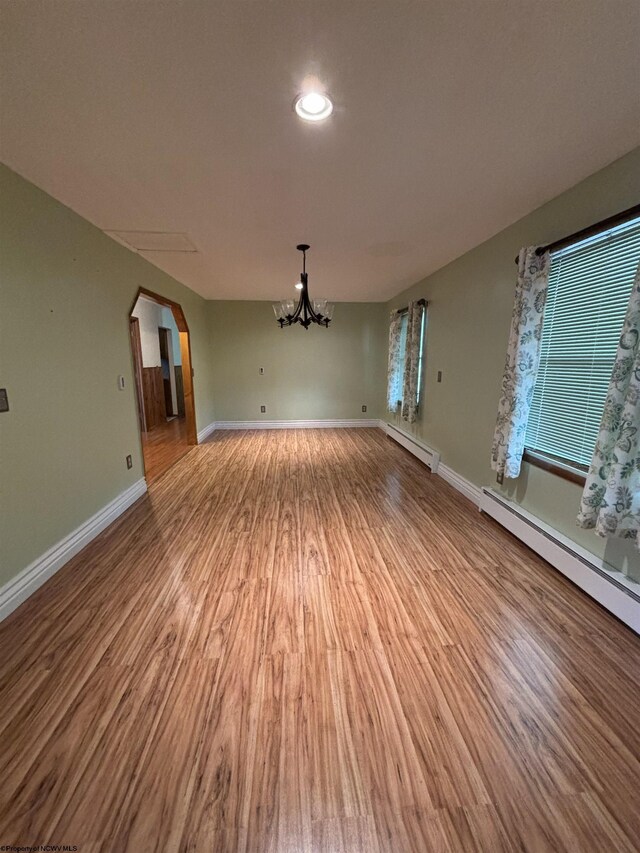 empty room with light hardwood / wood-style flooring, a baseboard radiator, and an inviting chandelier